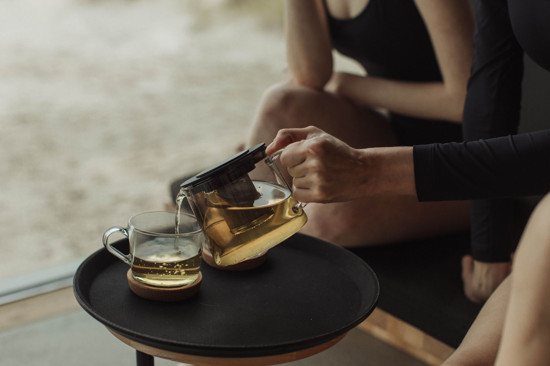 Pouring green tea from a glass teapot into a cup