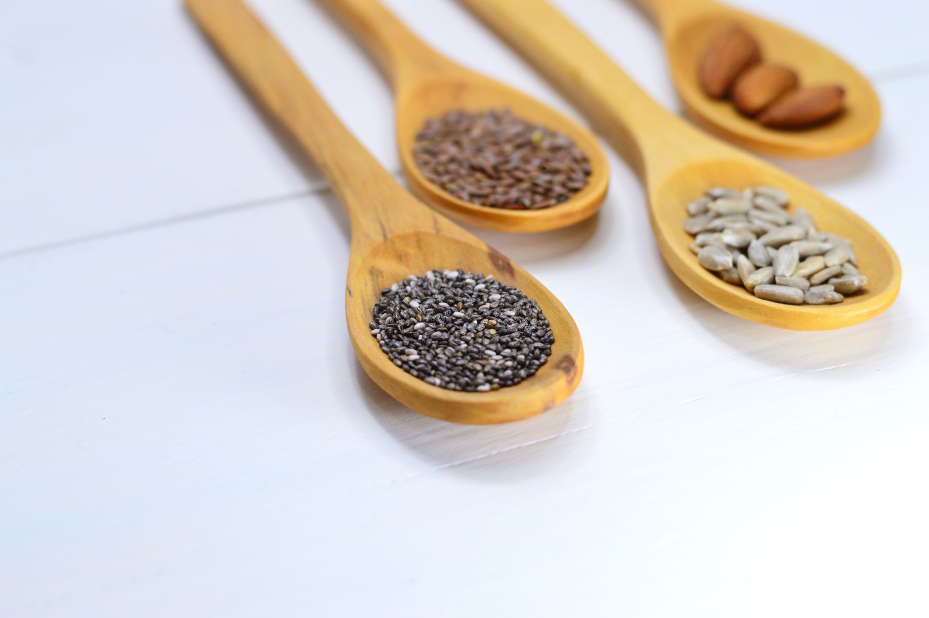 Chia, flax, sunflower seeds and almonds in wooden spoons