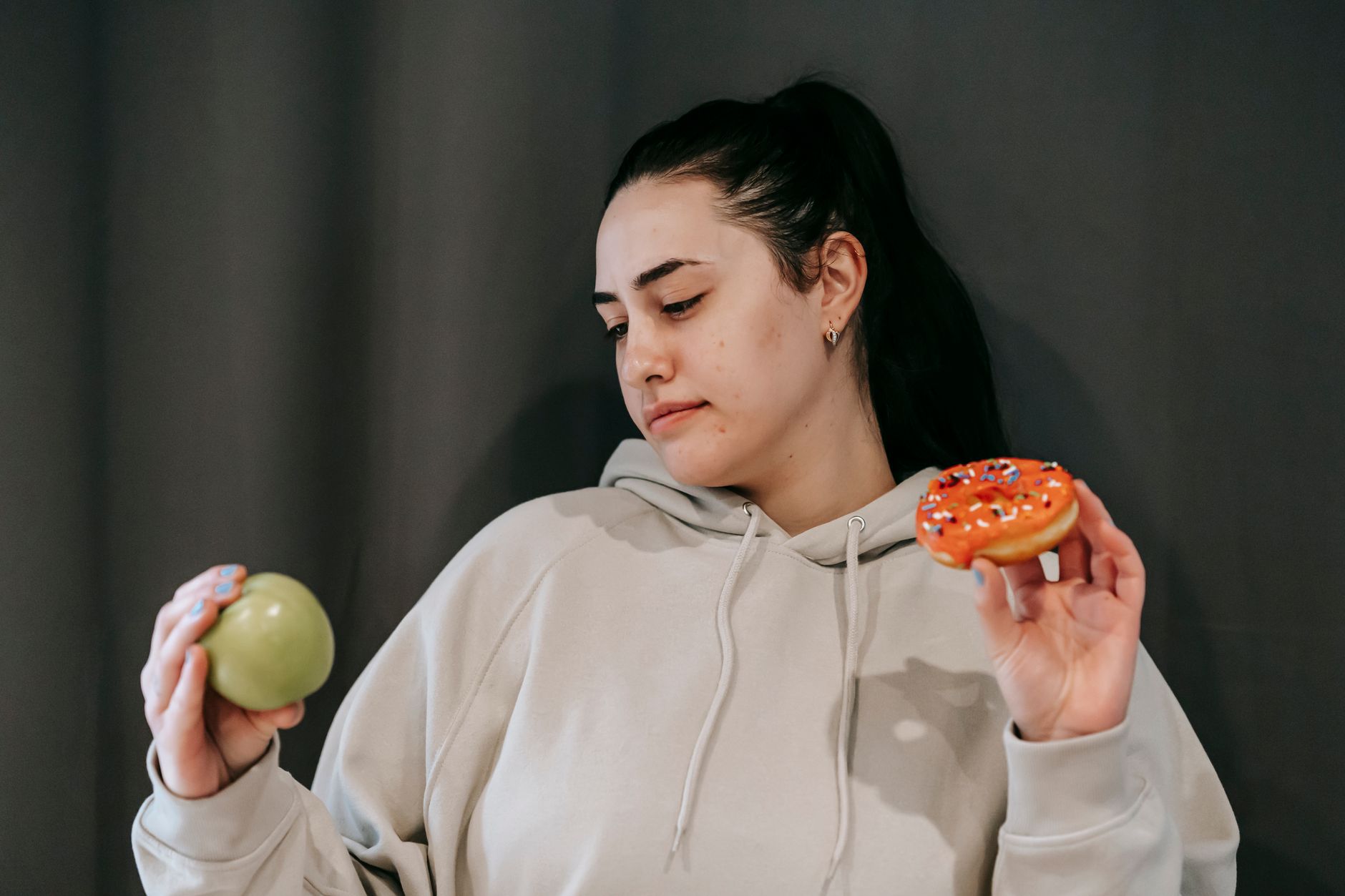 Woman choosing between a green apple and a frosted donut