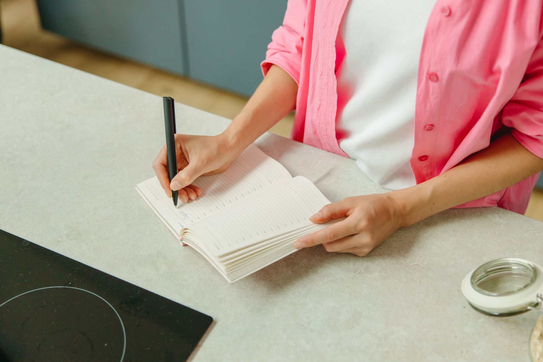 Woman writing in a food and symptom journal on a kitchen counter