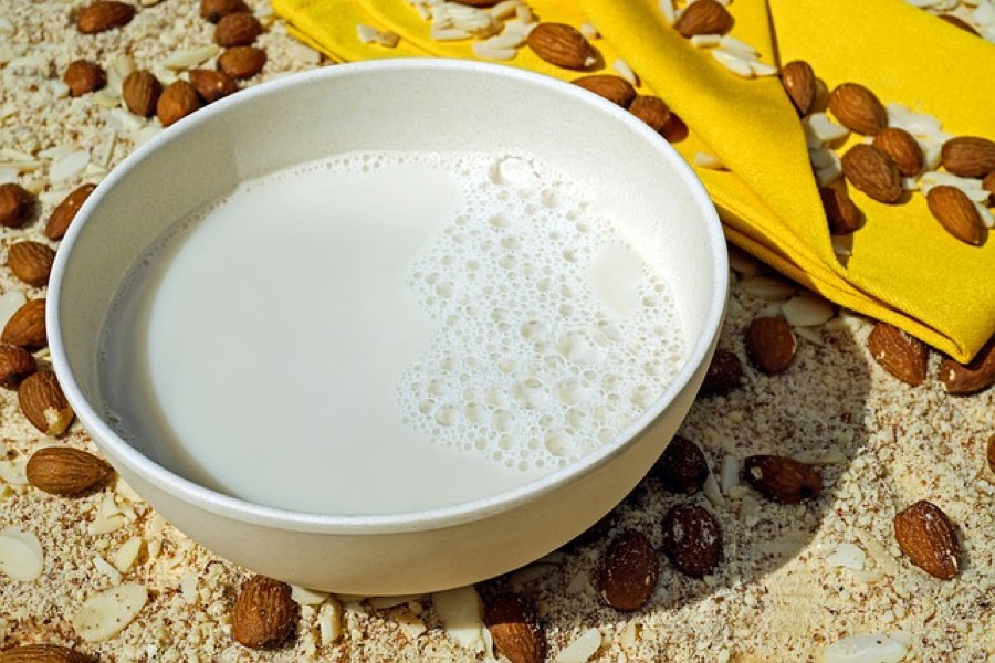 Bowl of almond milk surrounded by whole almonds, flaked almonds and almond meal
