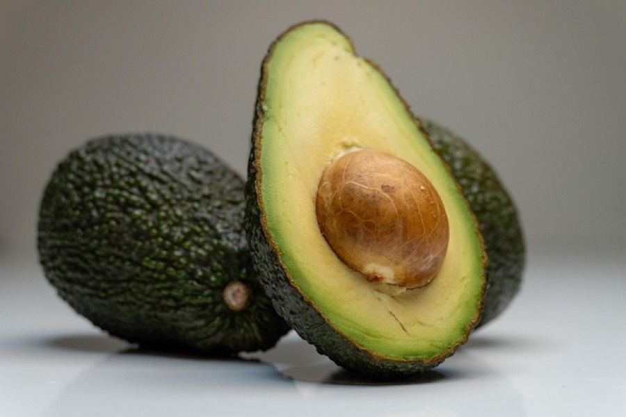 A whole dark green avocado next to a halved avocado showing its pale green flesh and stone