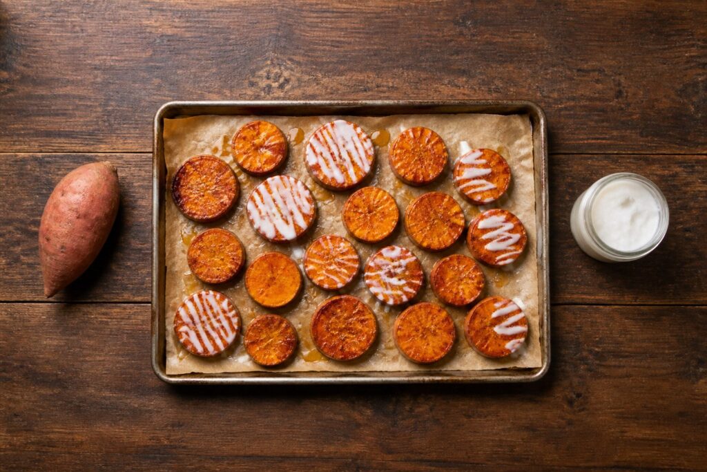 AIP baked cinnamon sweet potato rounds with coconut butter and honey drizzle on a parchment-lined sheet pan
