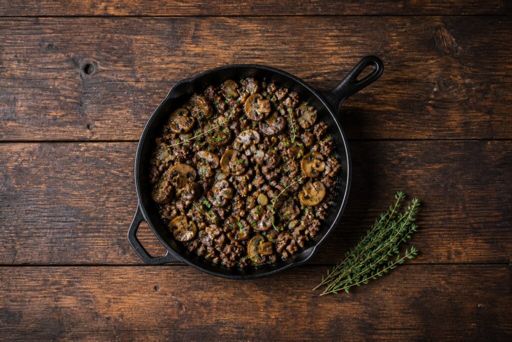 AIP ground beef and cremini mushroom skillet with fresh thyme and parsley in a cast iron pan