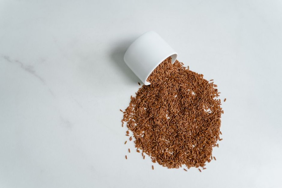 Uncooked brown rice grains spilling from a white cup onto a marble surface