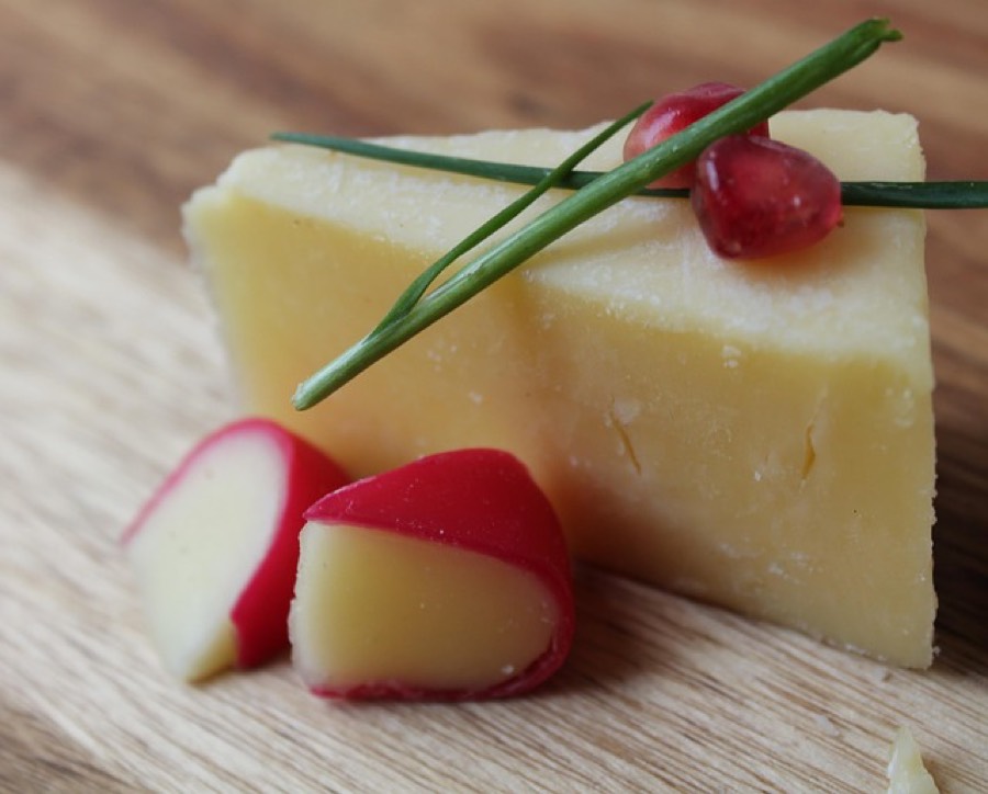 Wedge of aged hard cheese on a wooden board with radish and chives
