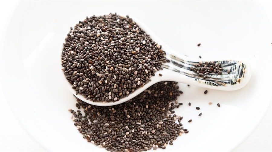 Raw black and white chia seeds heaped on a white ceramic spoon