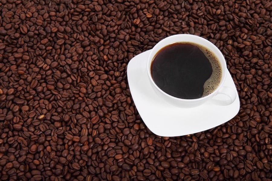 A white cup of black coffee on a saucer resting on a bed of roasted coffee beans