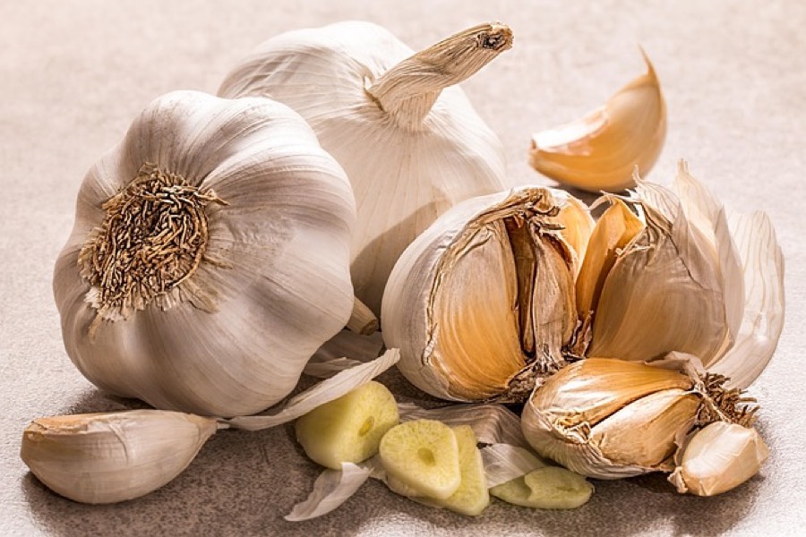 Whole garlic bulbs, peeled cloves and sliced garlic on a light stone surface