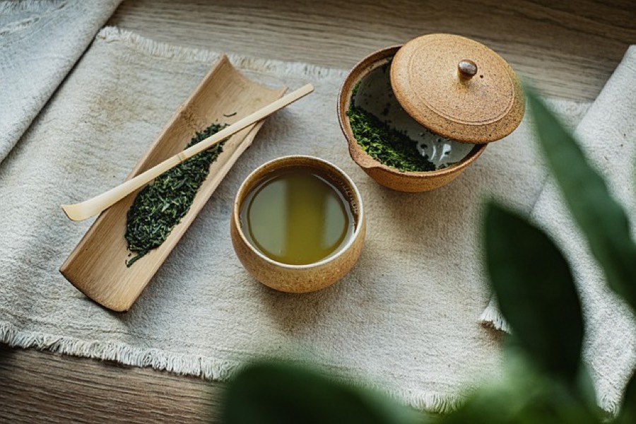 Cup of brewed green tea beside loose sencha leaves and a lidded clay teapot