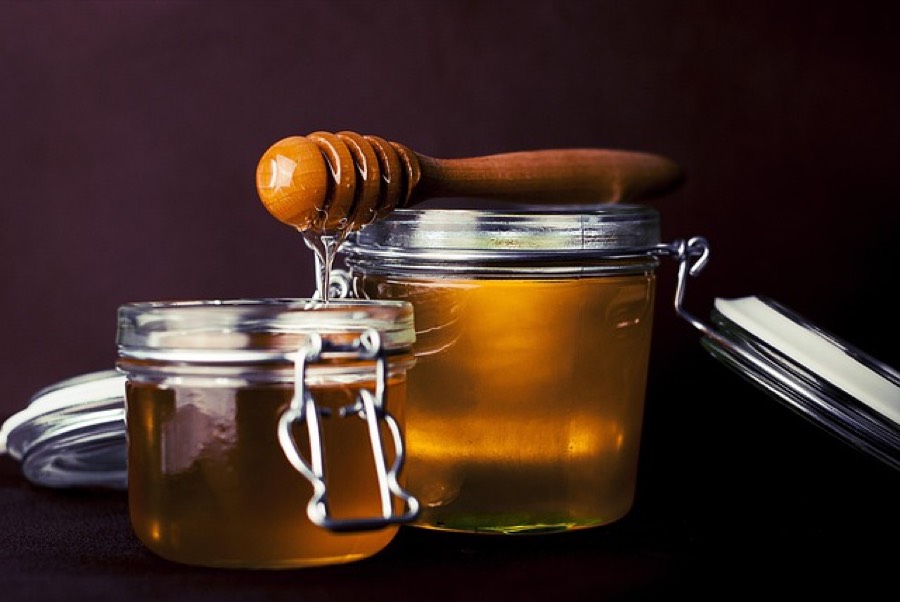 Two open glass jars of golden honey with a wooden honey dipper resting on top