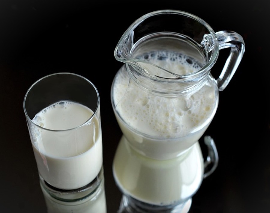 A glass of milk beside a glass jug of fresh milk on a dark reflective surface