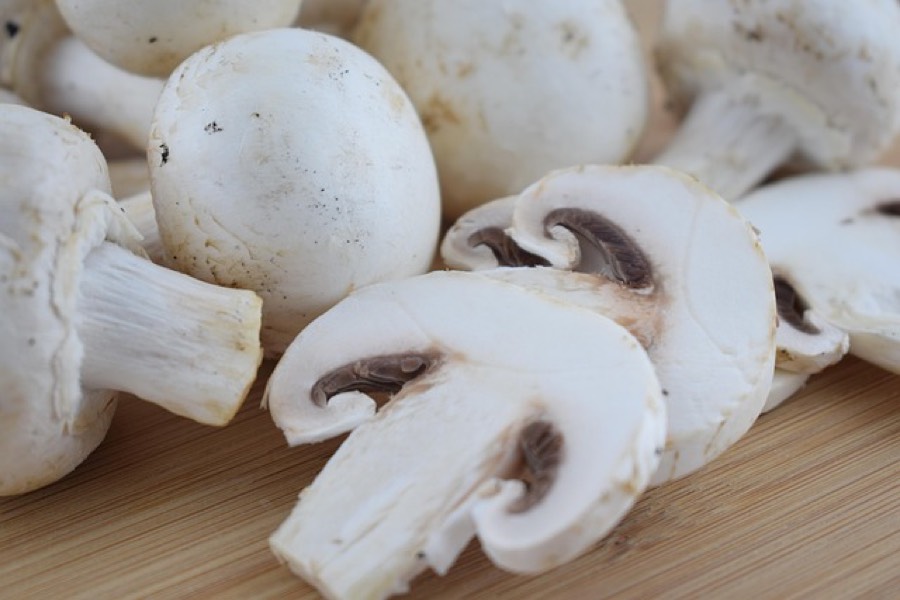 Fresh white button mushrooms, whole and sliced, on a wooden board