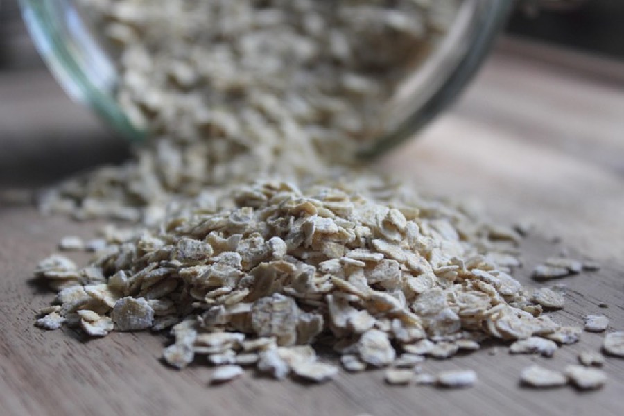 Plain rolled oats spilling from a glass jar onto a wooden board