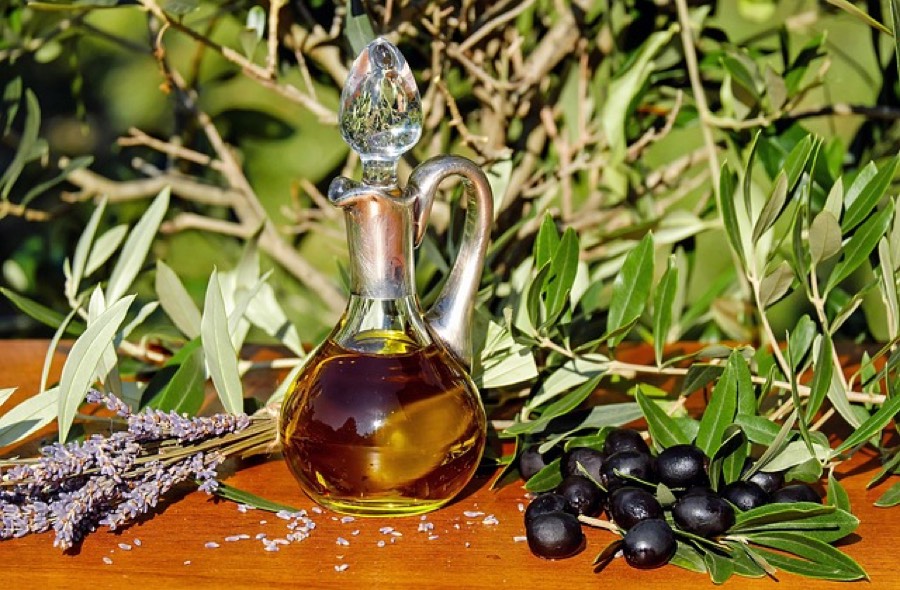 Glass carafe of extra virgin olive oil beside fresh olives and olive branches
