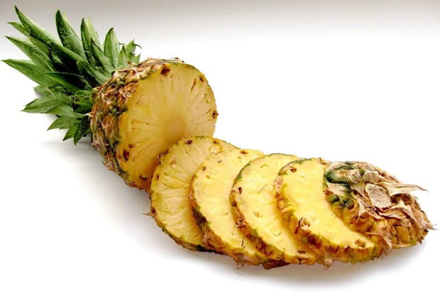 Fresh pineapple cut into slices next to the whole fruit
