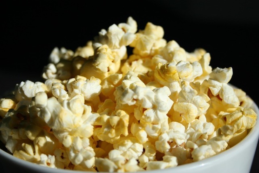 White bowl filled with freshly popped plain popcorn on a dark background