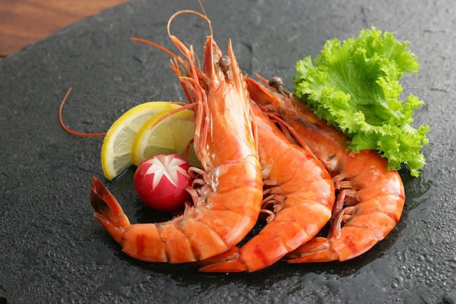 Cooked whole shrimp served on a dark slate plate with lemon wedges