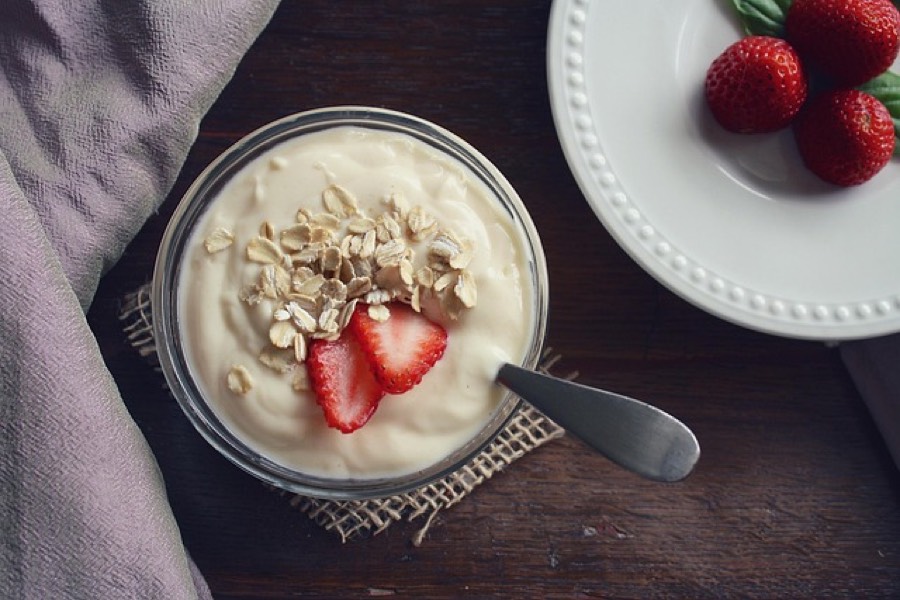 Glass bowl of plain yogurt topped with oats and sliced strawberry on a wooden table