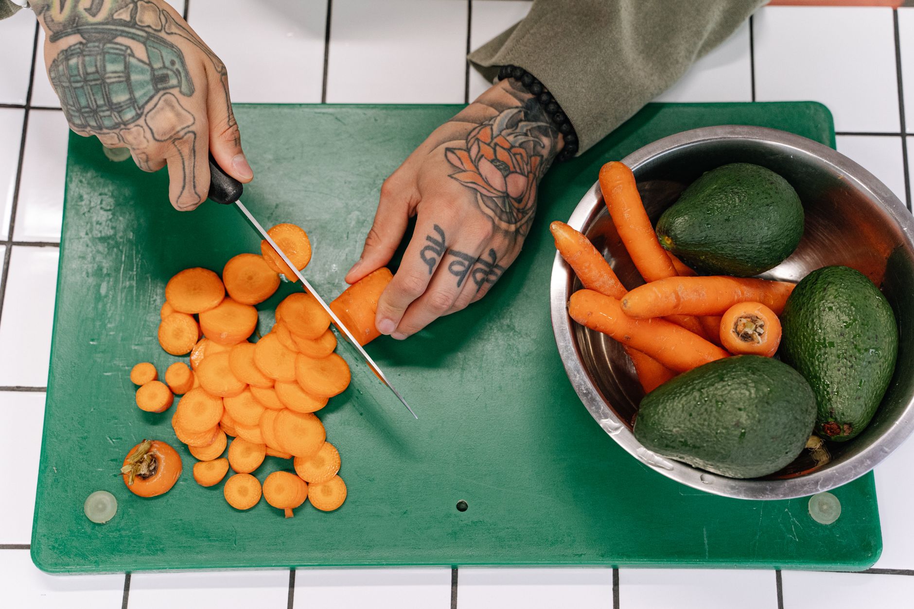 Slicing carrots on a cutting board next to a bowl of carrots and avocados for AIP meal prep