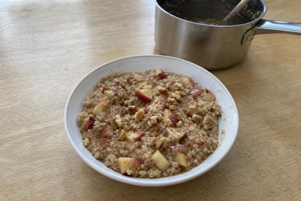 A deep bowl of steel-cut oatmeal with half-inch apple cubes stirred through, topped with roughly chopped toasted walnuts, the oats visibly grainy rather than smooth.
