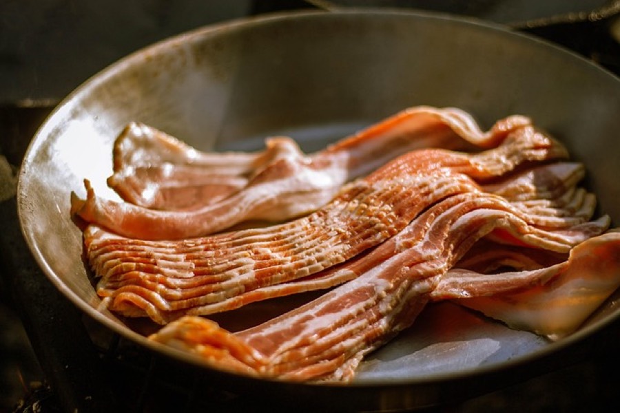 Raw streaky bacon rashers laid out in a metal frying pan
