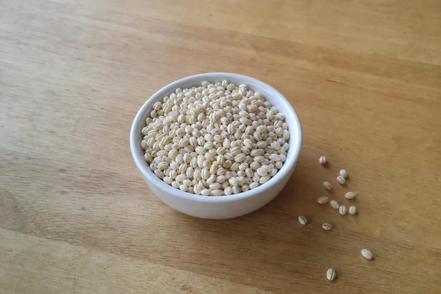 White bowl of dry pearl barley grains on a wooden table