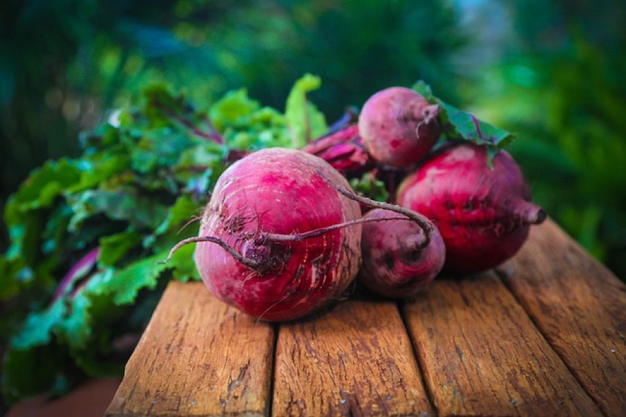 Fresh raw red beets with their leafy green tops on a wooden table