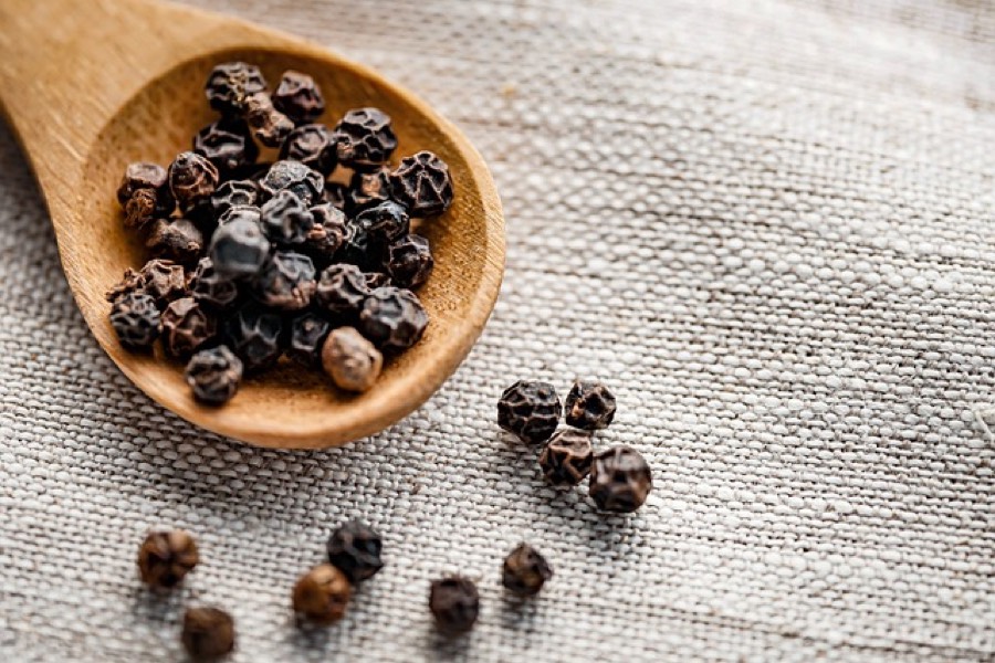 Whole black peppercorns in a wooden spoon on a linen cloth
