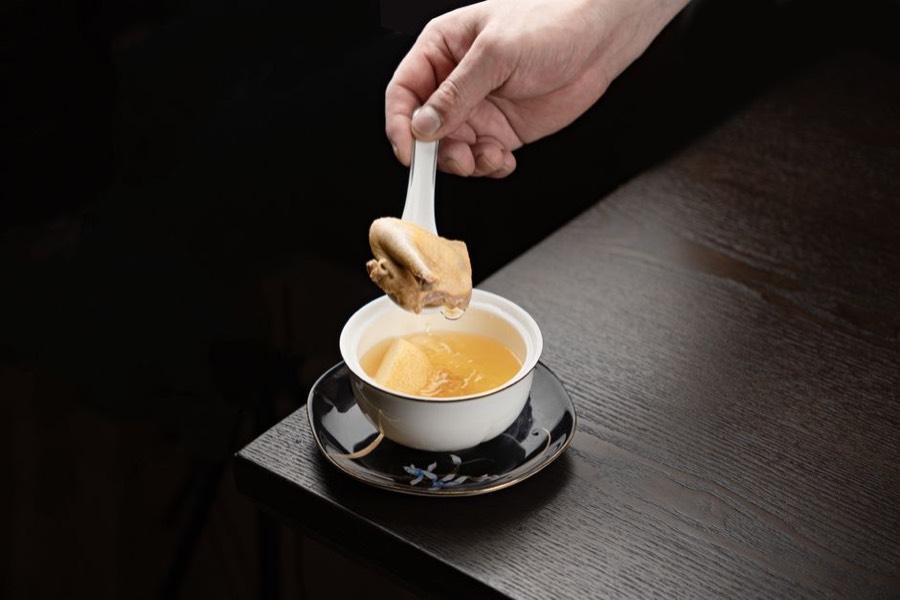 Bowl of golden chicken bone broth with a piece of poultry lifted out on a spoon