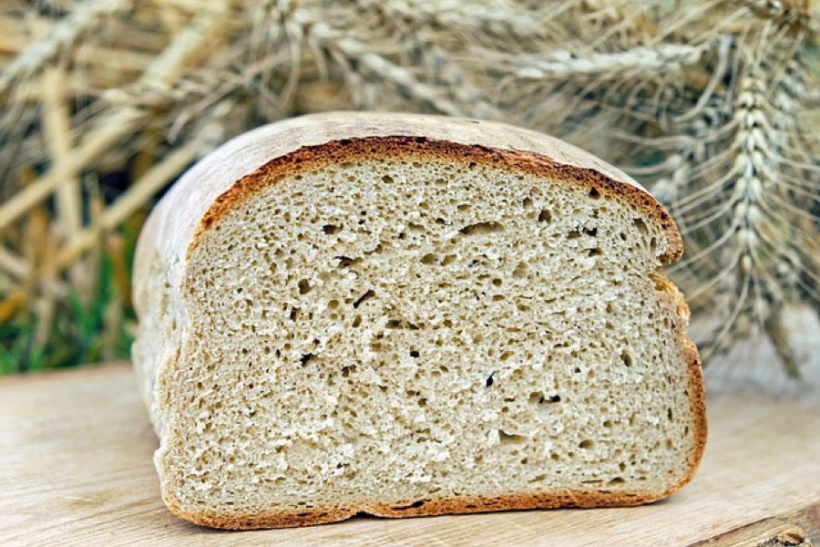 Half a loaf of white bread cut open to show the airy crumb, with ears of wheat behind it