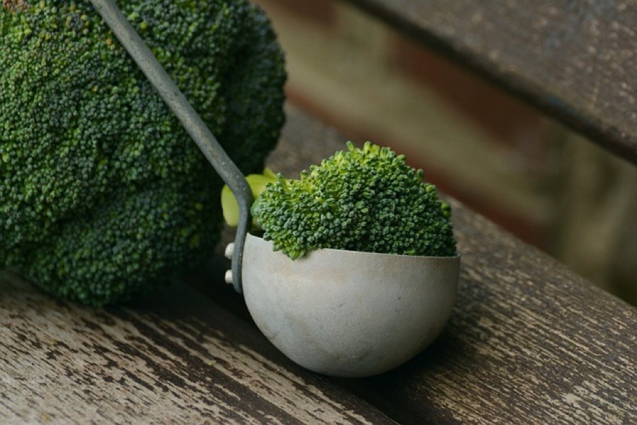 Fresh raw broccoli head with florets in a metal ladle on a wooden bench