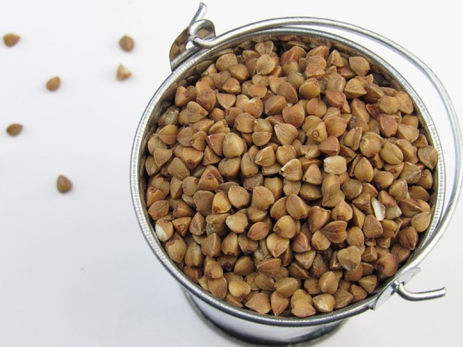 Raw buckwheat groats filling a small metal pail on a white surface