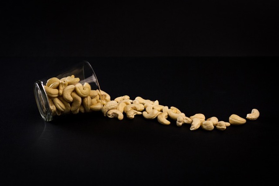 Whole raw cashew nuts spilling from a glass jar onto a dark surface