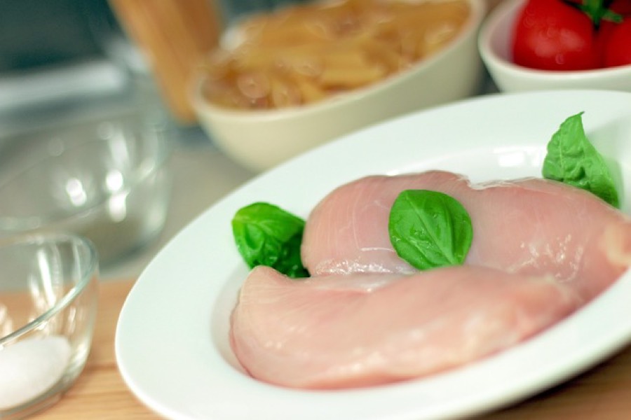 Raw skinless chicken breast fillets on a white plate with fresh basil leaves