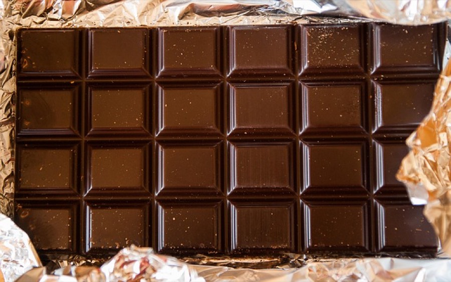 An unwrapped bar of chocolate divided into squares, lying on gold foil