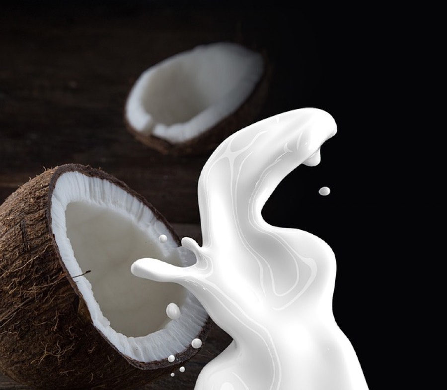 Coconut milk pouring out of a fresh cracked coconut half on a dark wooden background