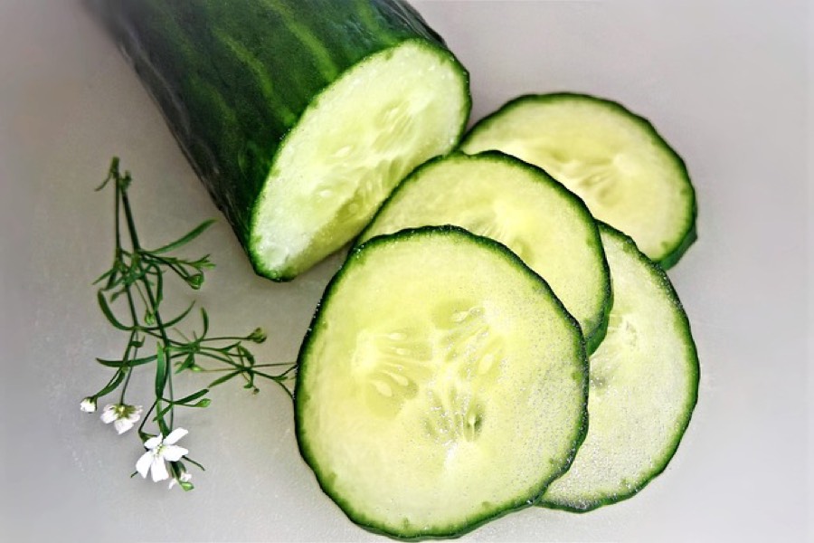 Whole cucumber with three slices cut from the end, showing the dark green skin and pale seeded flesh