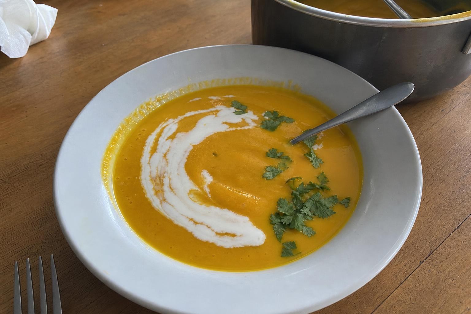Bowl of smooth deep-orange ginger turmeric carrot soup with a swirl of coconut milk and scattered cilantro leaves, spoon resting in the bowl