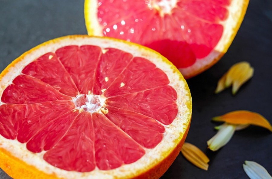 Two halves of a pink grapefruit on a dark surface, showing the red segments and the white pith