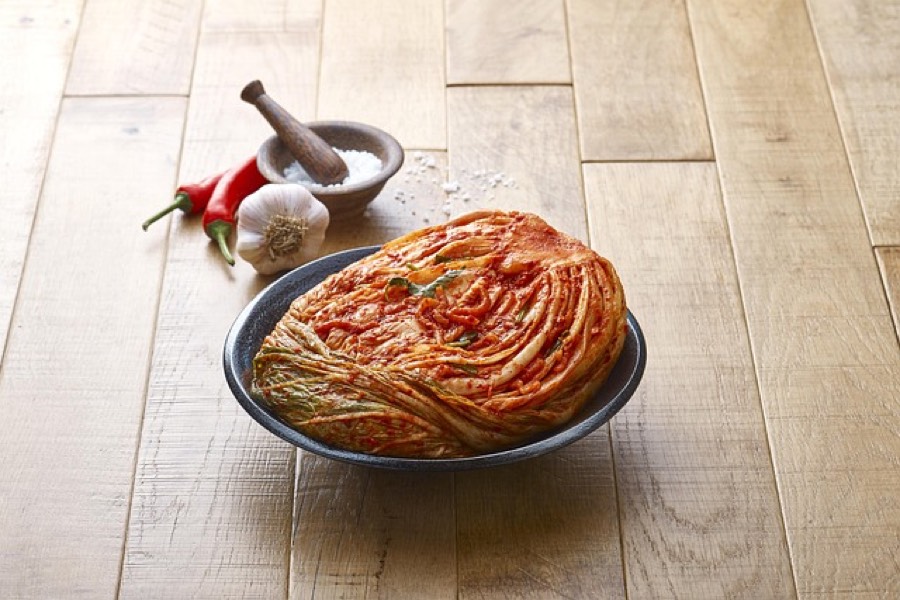 Whole napa cabbage kimchi in a dark bowl, with red chilli, garlic and salt beside it
