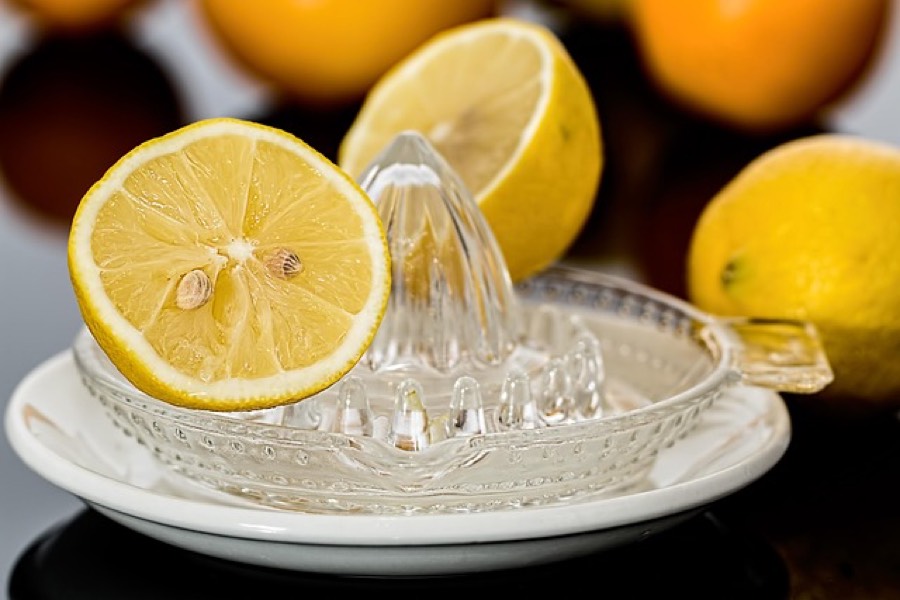 Half a lemon on a glass juicer with whole lemons behind it