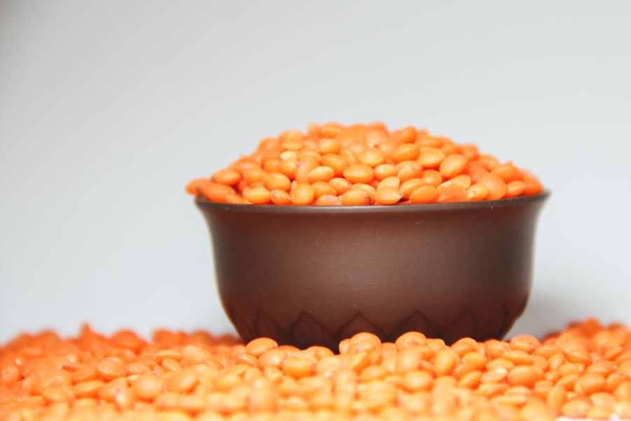 A small bowl of dried red lentils with more lentils spread around it