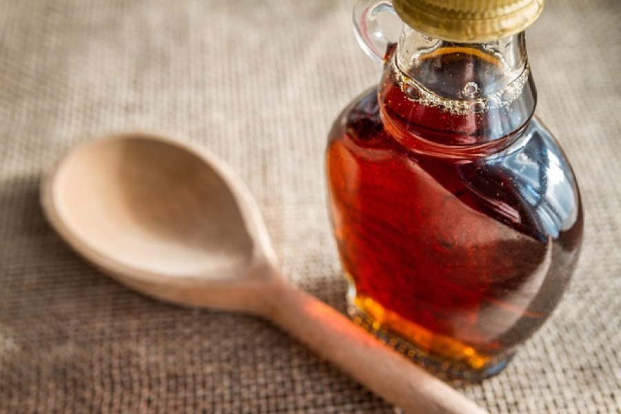 Glass bottle of dark amber maple syrup beside a wooden spoon on burlap