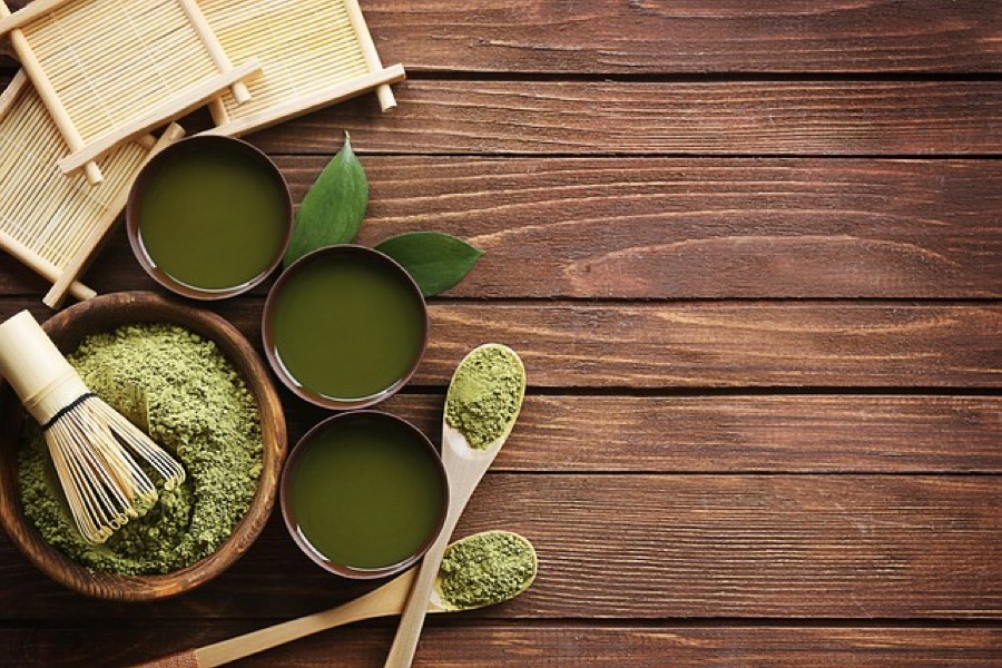 Matcha powder in a wooden bowl with a bamboo whisk and three cups of whisked matcha