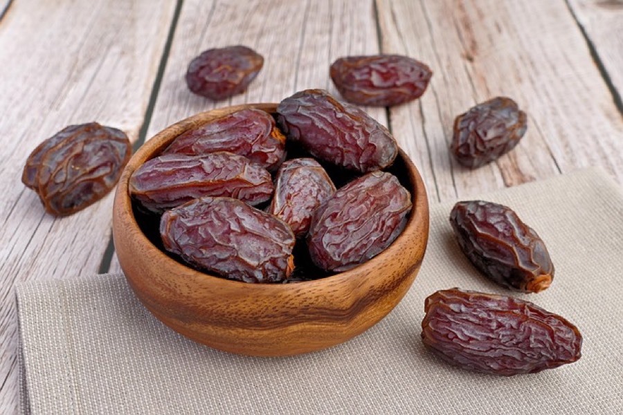 Whole Medjool dates in a wooden bowl on a light wooden table