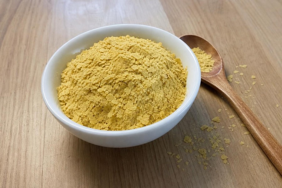 Bowl of pale yellow nutritional yeast flakes with a wooden spoon on a wooden table