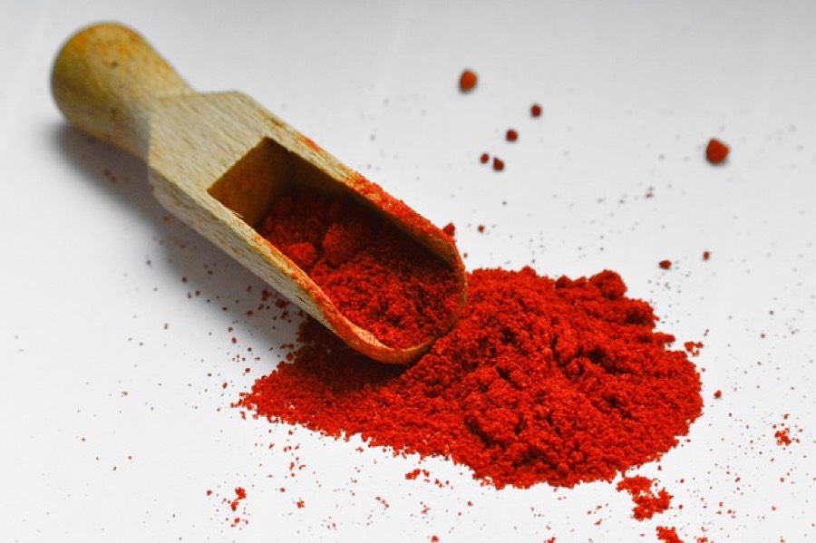 Ground red paprika spilling from a wooden scoop onto a white surface