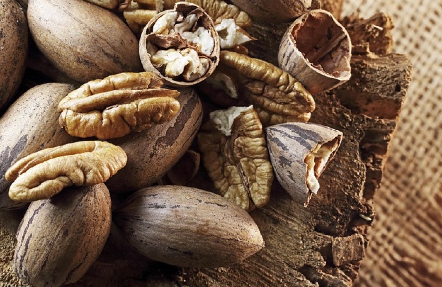 Whole pecans in their shells and shelled pecan halves on a rustic wooden surface