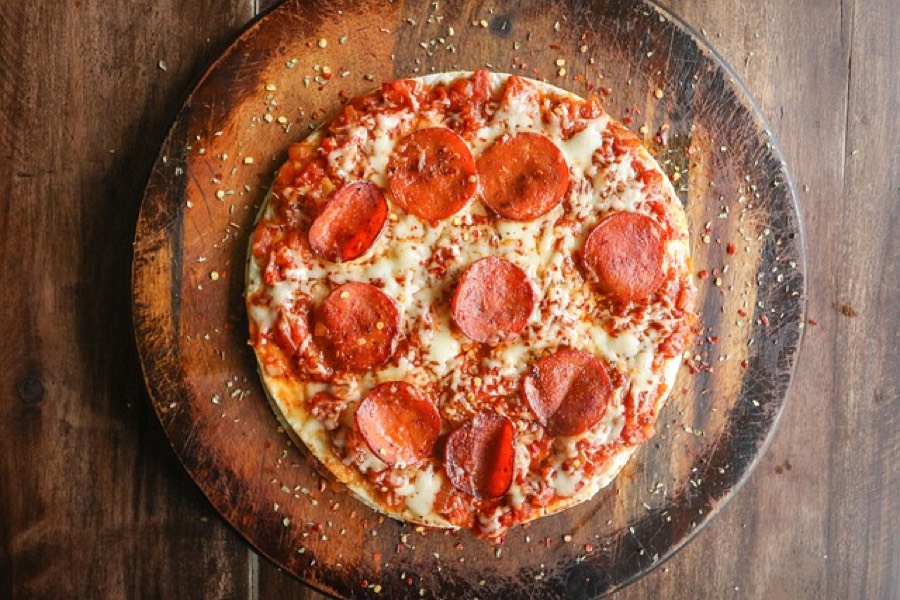 Whole pepperoni pizza on a wooden board, seen from above with chilli flakes scattered around